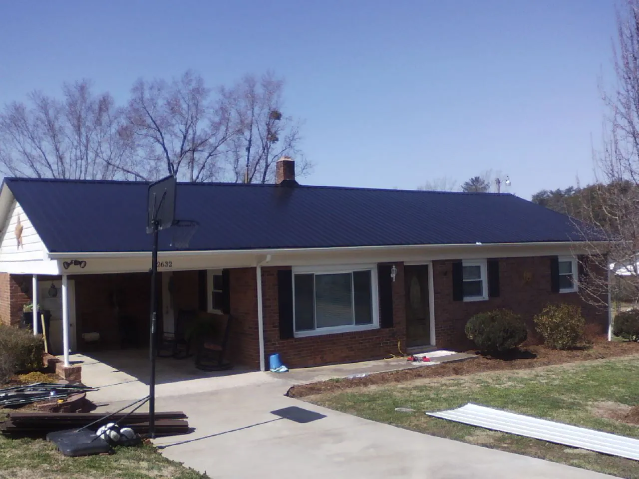 Finished dark blue metal roof on a brick ranch with a carport in Dansville