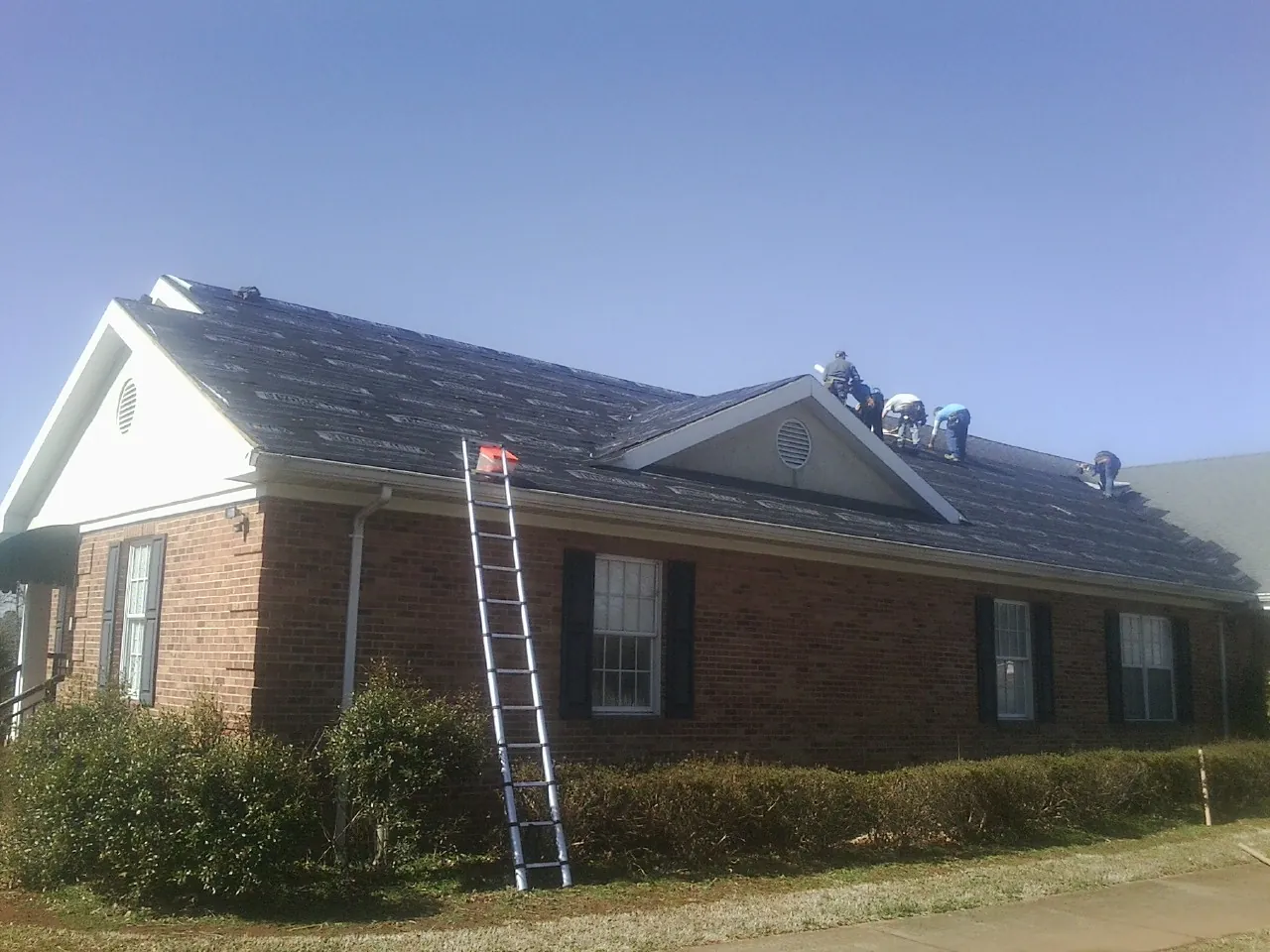 Crew tearing shingles off a brick ranch roof with a ladder set — Emergency Roof Repair work by our crew in Dansville