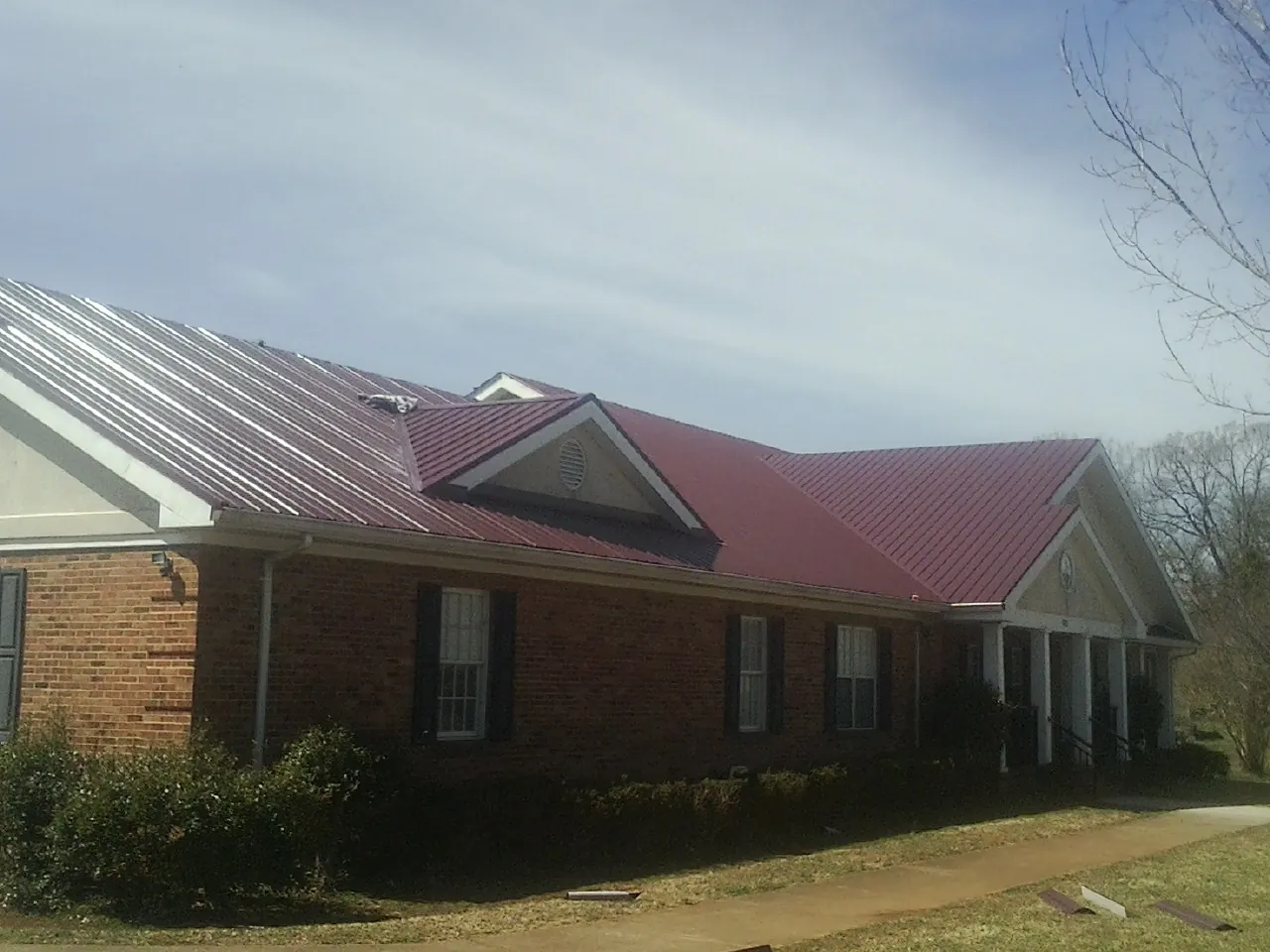 Red metal roof with gabled entries on a long brick building, from a Hail Damage Roof Repair job in Dansville