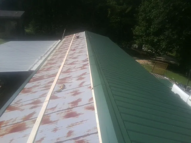 Old rusted panels beside newly installed green metal roofing — Wind Damage Roof Repair by Roofing Brothers in Dansville