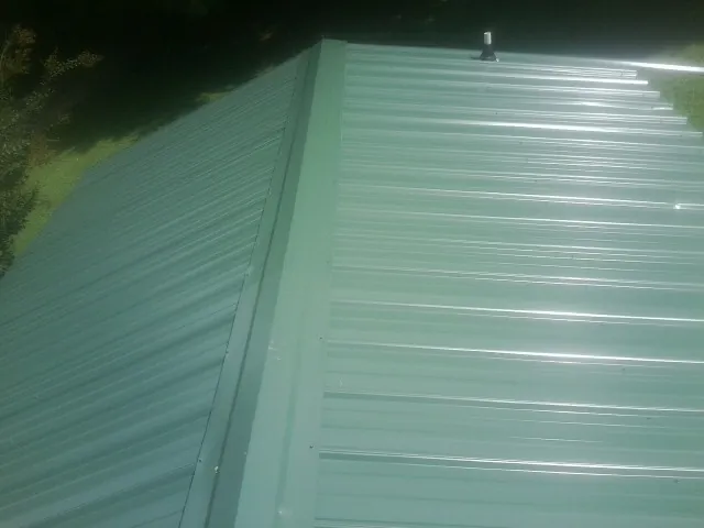New green metal panels meeting at the ridge of a roof — Flat Roof Repair work by our crew in Dansville