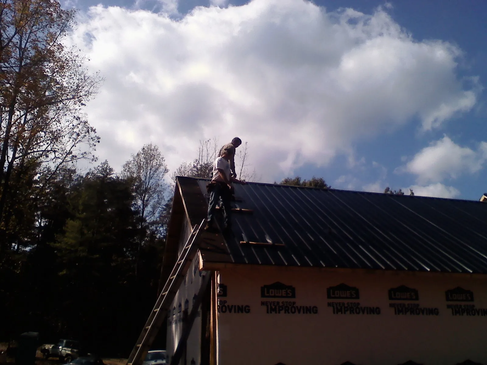Roofer fastening dark metal panels high against a cloudy sky, from a Roof Inspection job in Dansville