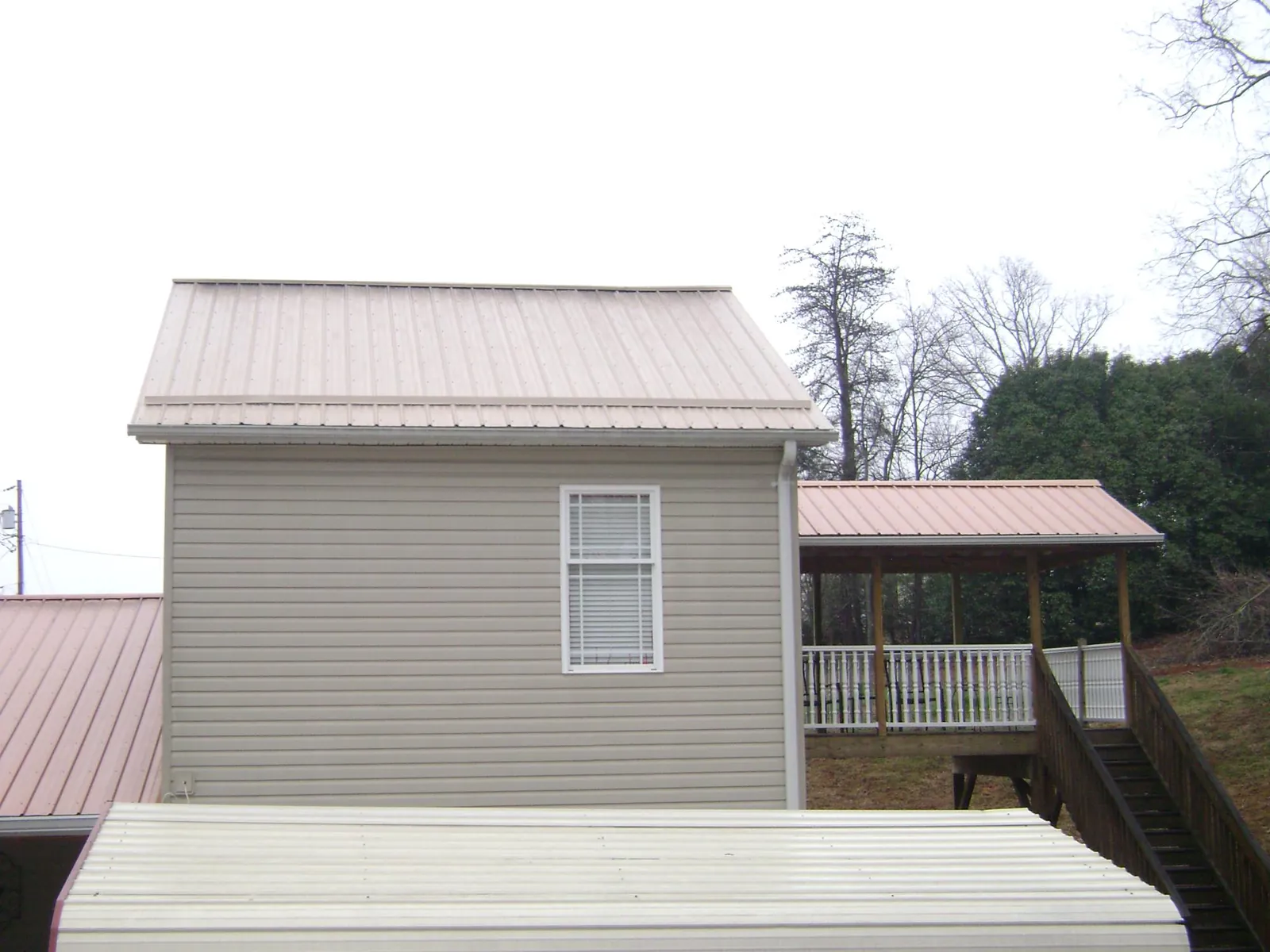 Tan metal roofs on a two story addition and attached porch, from a Roof Replacement job in Dansville